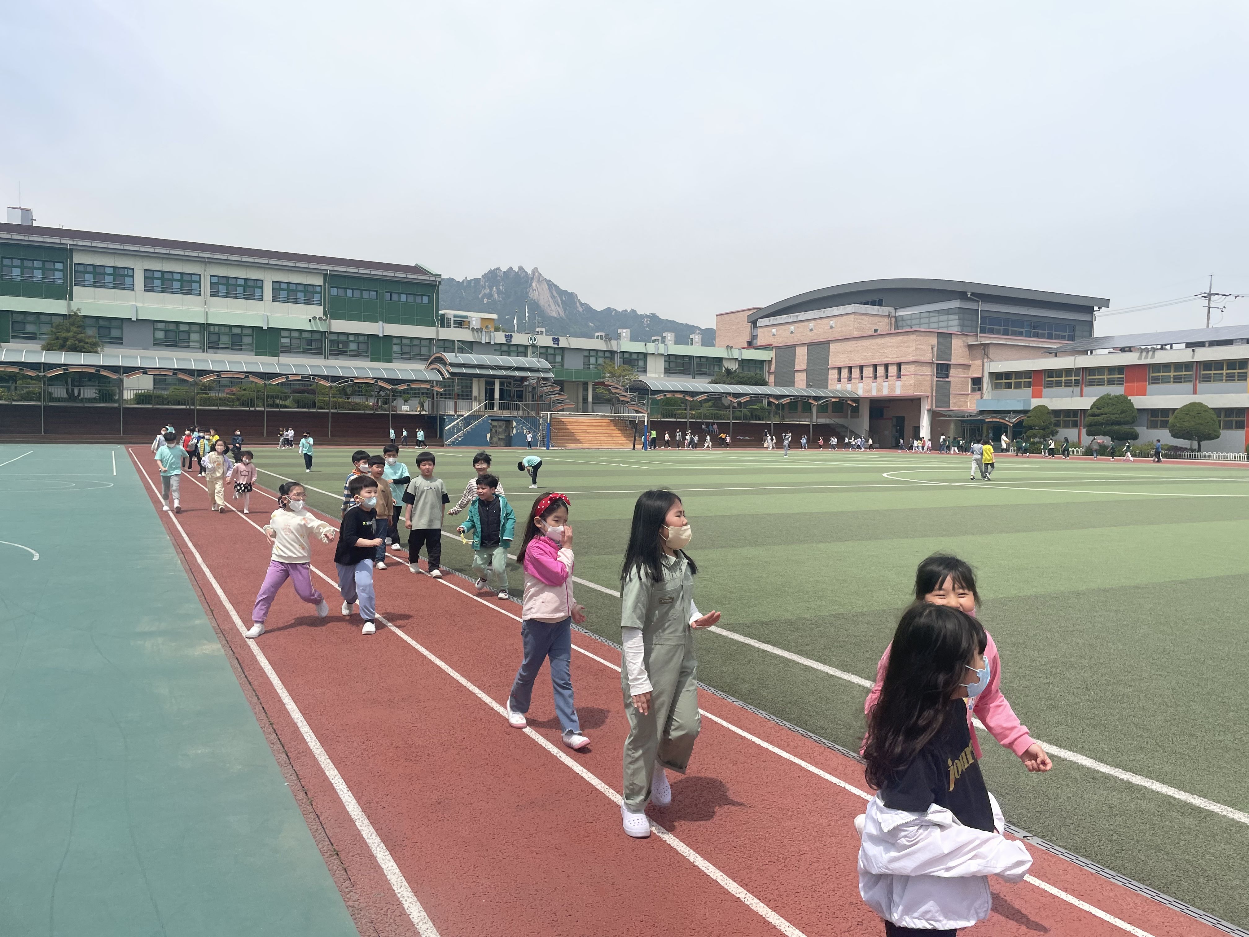 어린아이들이 운동장 트랙을 걷고 뛰며 운동하는 모습